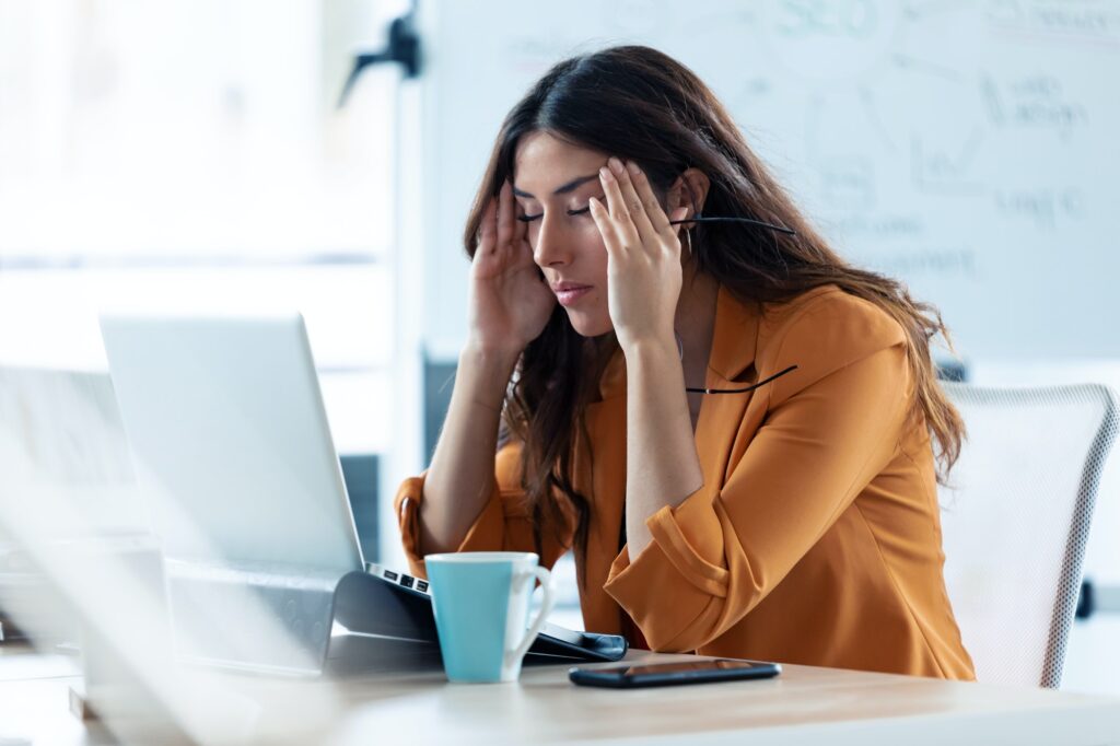 Giovane donna d'affari con mal di testa che lavora con il computer portatile in ufficio.