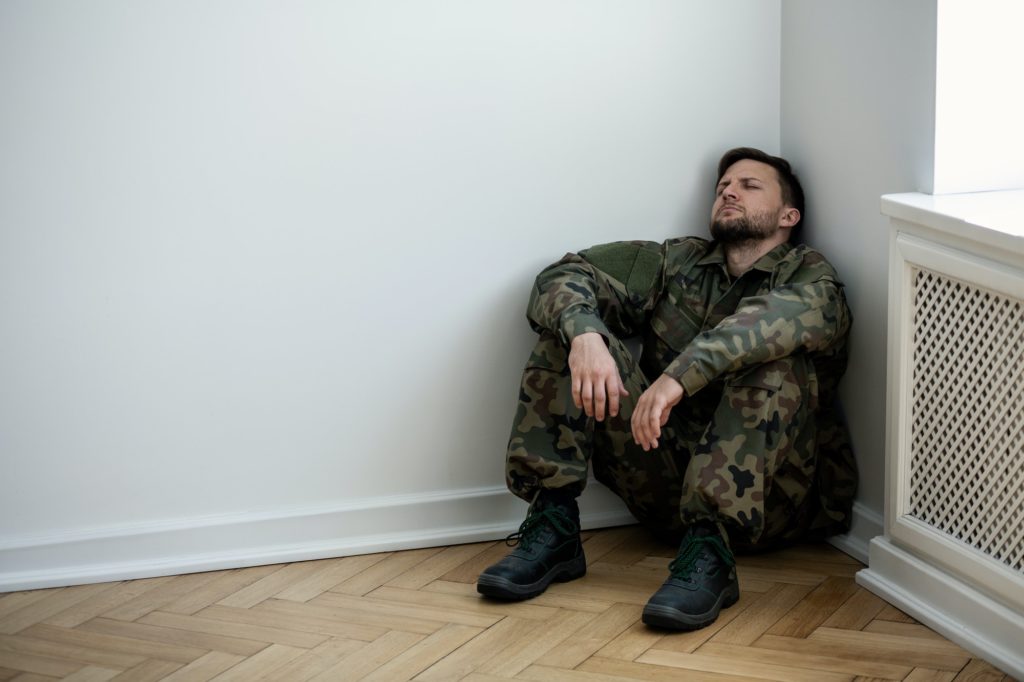 Uomo dell'esercito depresso in uniforme seduto in un angolo di una stanza vuota